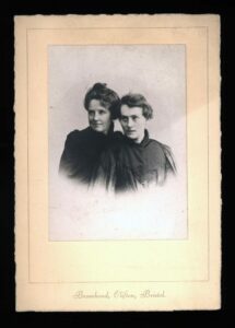 portrait of two women dressed in black. Woman on the left wears her hair up on her head, woman on the right has short hair